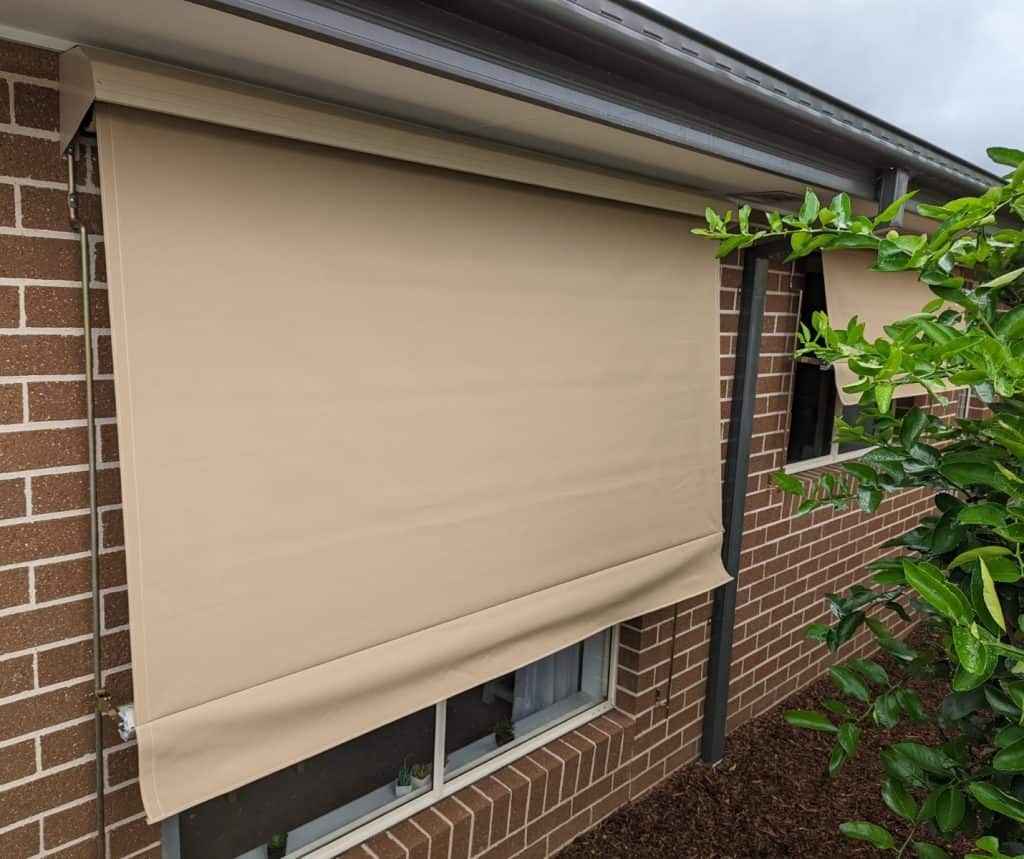 Showing beige spring loaded awnings shading a brick home’s windows.
