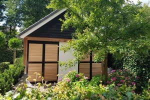 Showing cedar outdoor shutters on garden shed with flowering plants in foreground