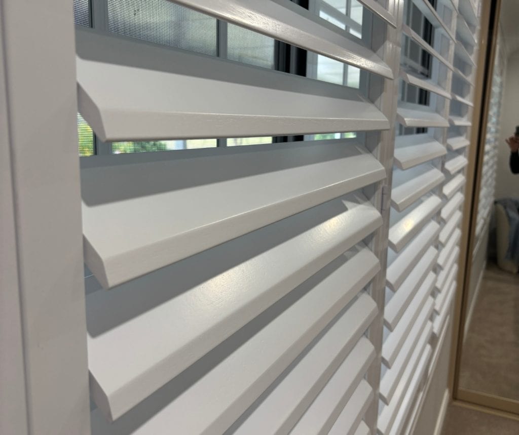 Showing a close-up of white heritage timber shutters with bevelled louvres and smooth finish.