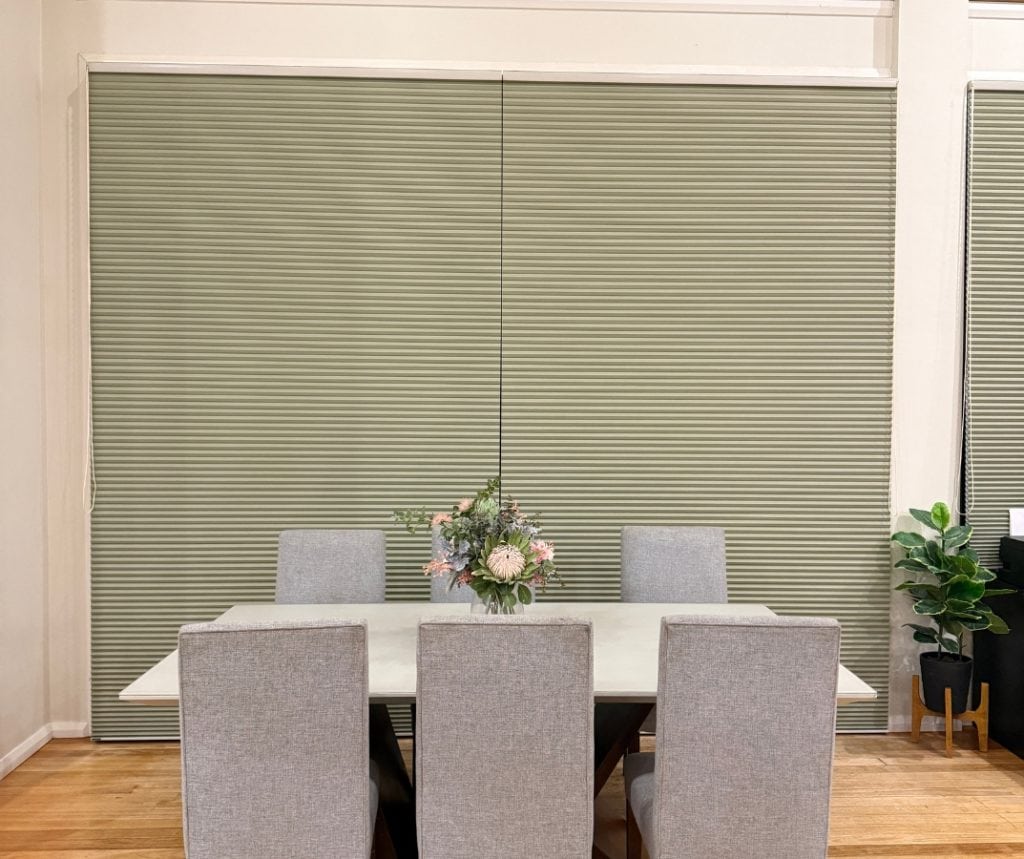 Showing a dining room with full-height olive honeycomb blinds closed behind chairs.