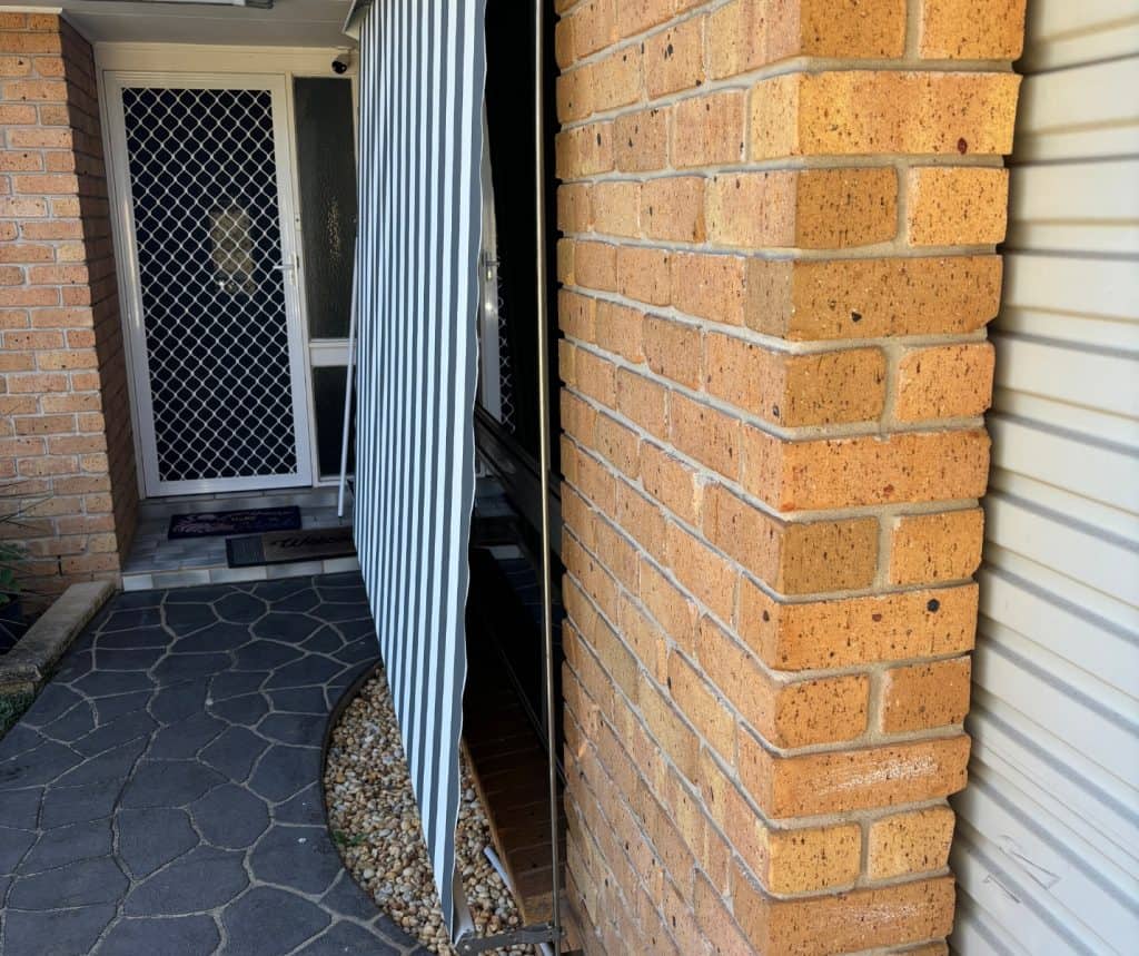 Showing entryway window spring awning providing shade at brick home.