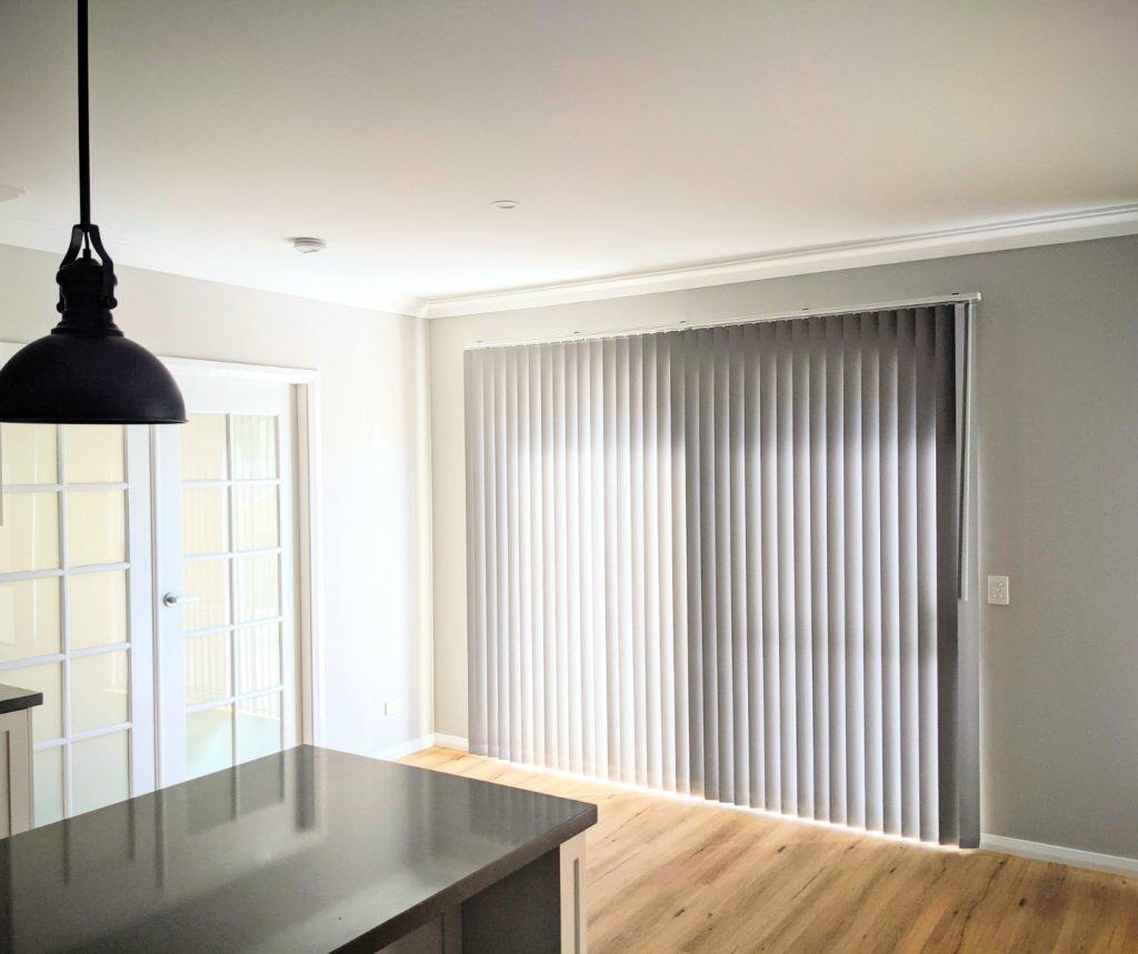 Showing kitchen vertical blinds across large windows with soft filtered light.
