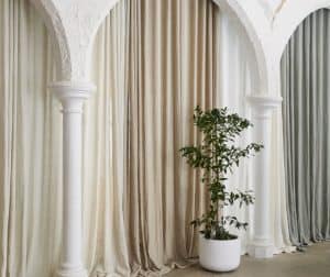 Displaying neutral-toned blockout curtains hung behind arches with soft natural drape and indoor plant.