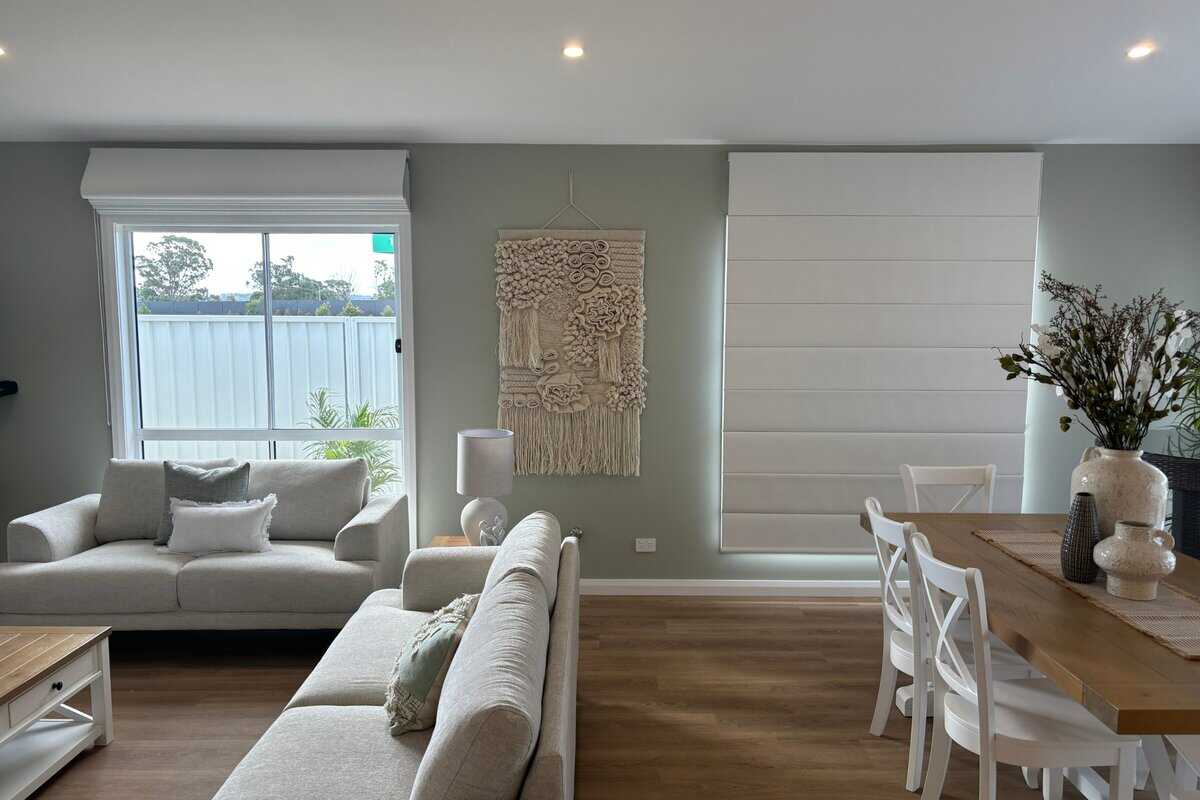 Showing roman blinds in a modern living room with soft light and neutral décor for refined comfort.