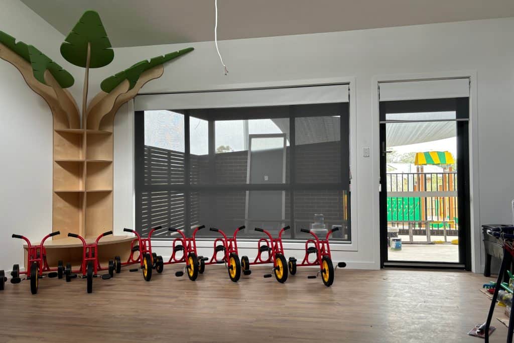 Showing child-safe blinds in a bright school room with red tricycles neatly lined up.