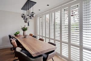 Showing white teak shutters in a dining room with natural timber table and soft light.