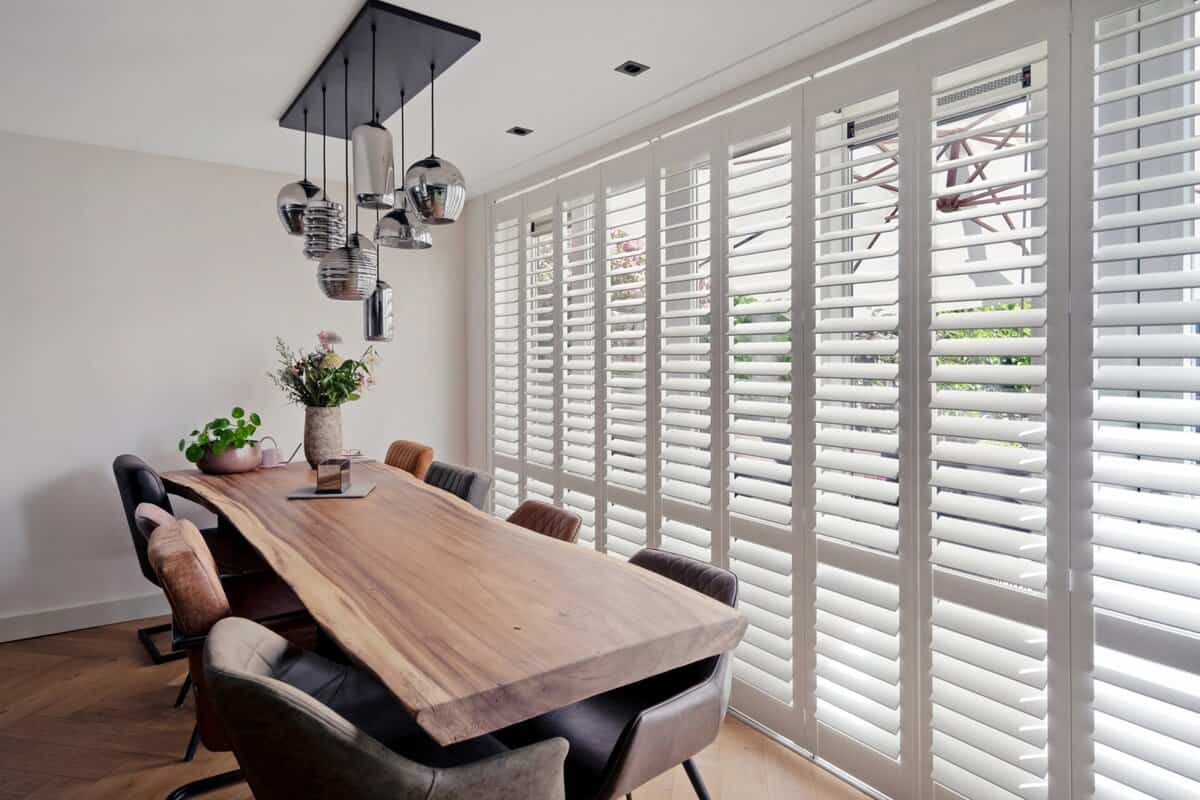 Showing white teak shutters in a dining room with natural timber table and soft light.