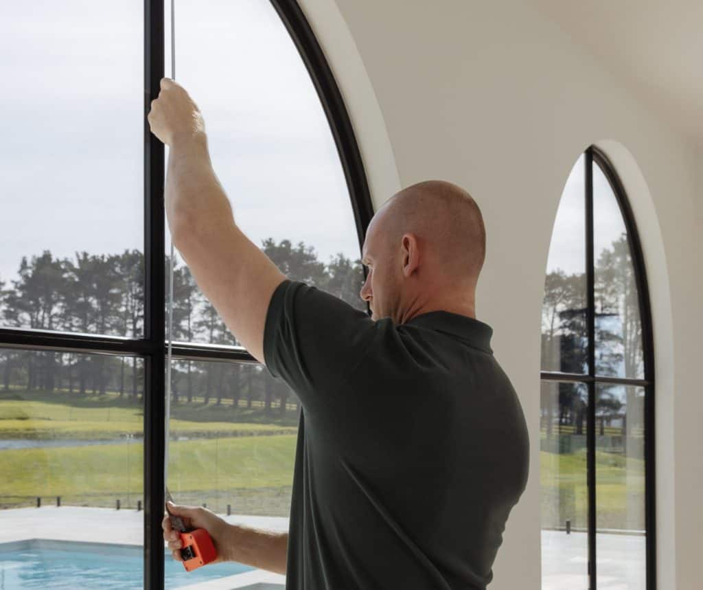 Showing a tradesperson measuring a large arched window for a commercial fitout.