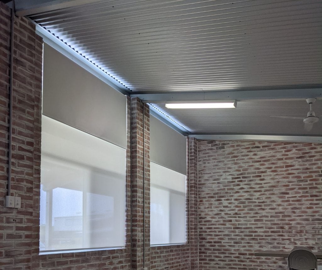 Showing commercial roller blinds in a brick interior with natural light filtering through top-down coverings