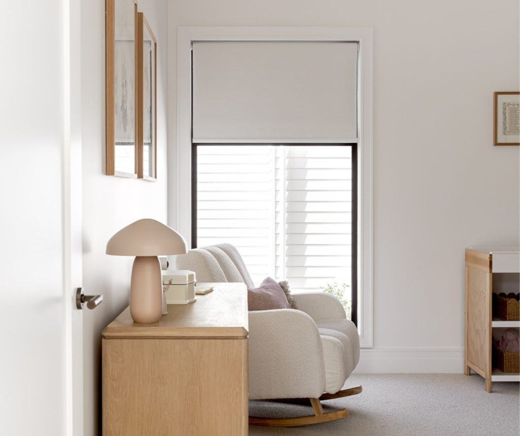 Showing smart nursery window blind partially lowered over tall frame in soft-toned baby room setup