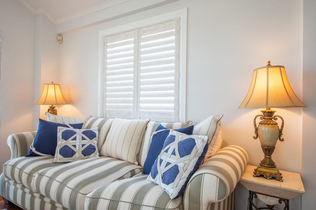 Showing white teak shutters in a lounge room with striped sofa, blue cushions, and traditional lamps