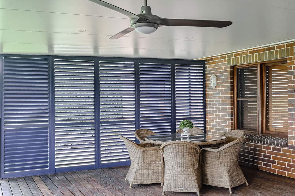 Showing Ocean Blue aluminium plantation shutters enclosing an alfresco entertaining area, providing shade, privacy and airflow.