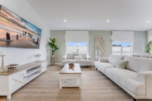 Showing a bright living room with white Roman blinds, neutral sofas, timber flooring and soft natural light throughout.
