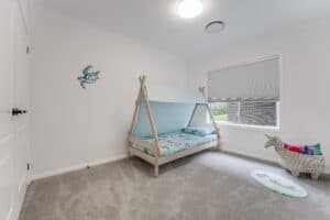 Showing a children's bedroom with custom cellular blinds, soft carpeting, a timber bed frame and filtered natural light.