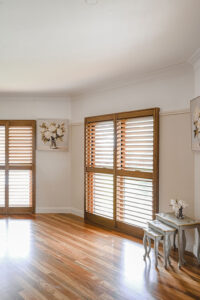 Showing real timber heritage window shutters with a natural woodgrain finish, providing light control in a timeless living room.