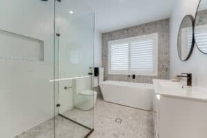 Showing white plantation shutters in a modern bathroom with a freestanding bath, tiled finishes and natural light.