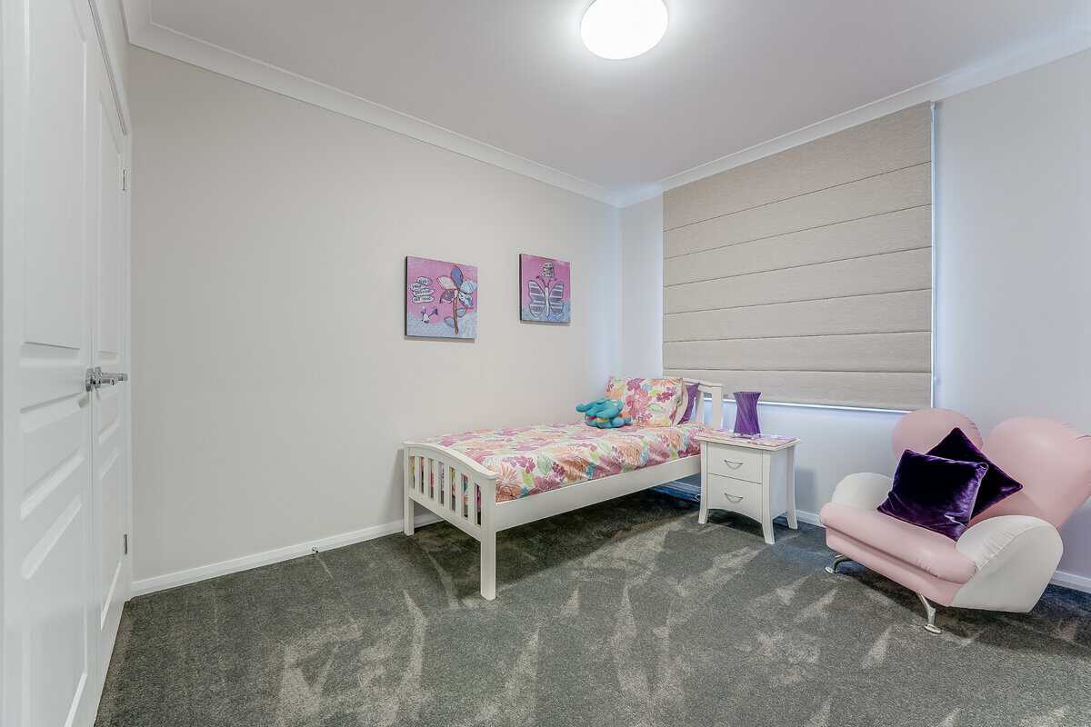 Showing a girl's bedroom with neutral Roman blinds, soft furnishings, plush carpet and gentle natural light.