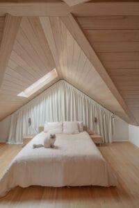 Custom blockout curtains fitted to a triangular bedroom window beneath a vaulted timber ceiling, providing privacy and complete light control.