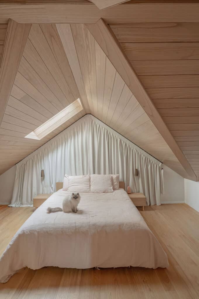 Custom blockout curtains fitted to a triangular bedroom window beneath a vaulted timber ceiling, providing privacy and complete light control.