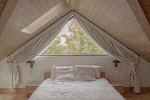 Custom blockout curtains frame a triangular window above the bed in a modern master bedroom, providing privacy and light control.
