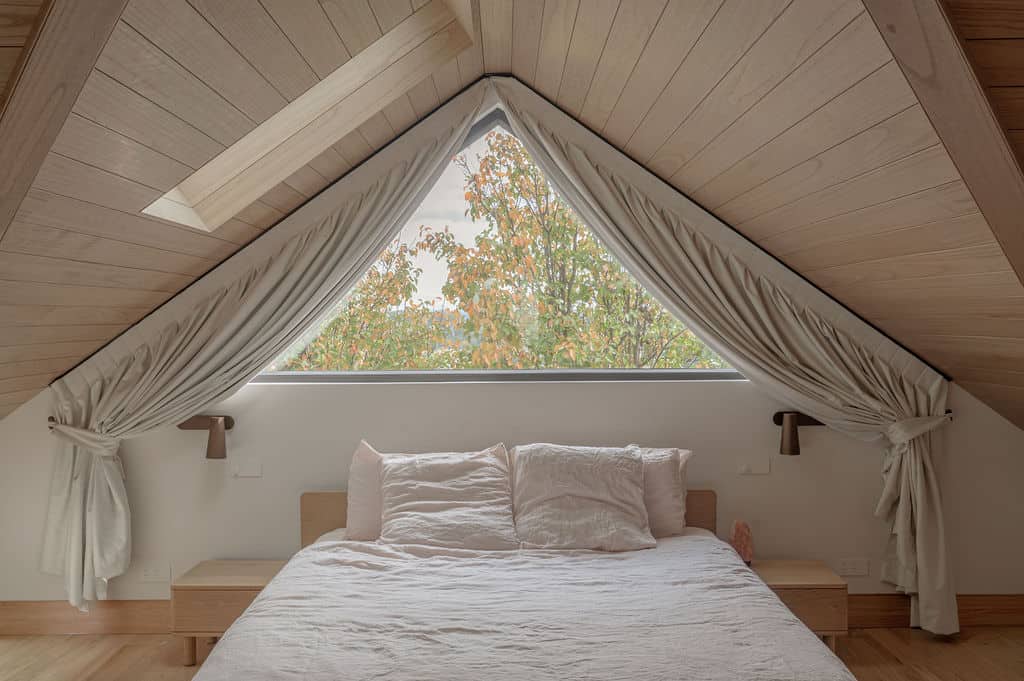 Custom blockout curtains frame a triangular window above the bed in a modern master bedroom, providing privacy and light control.