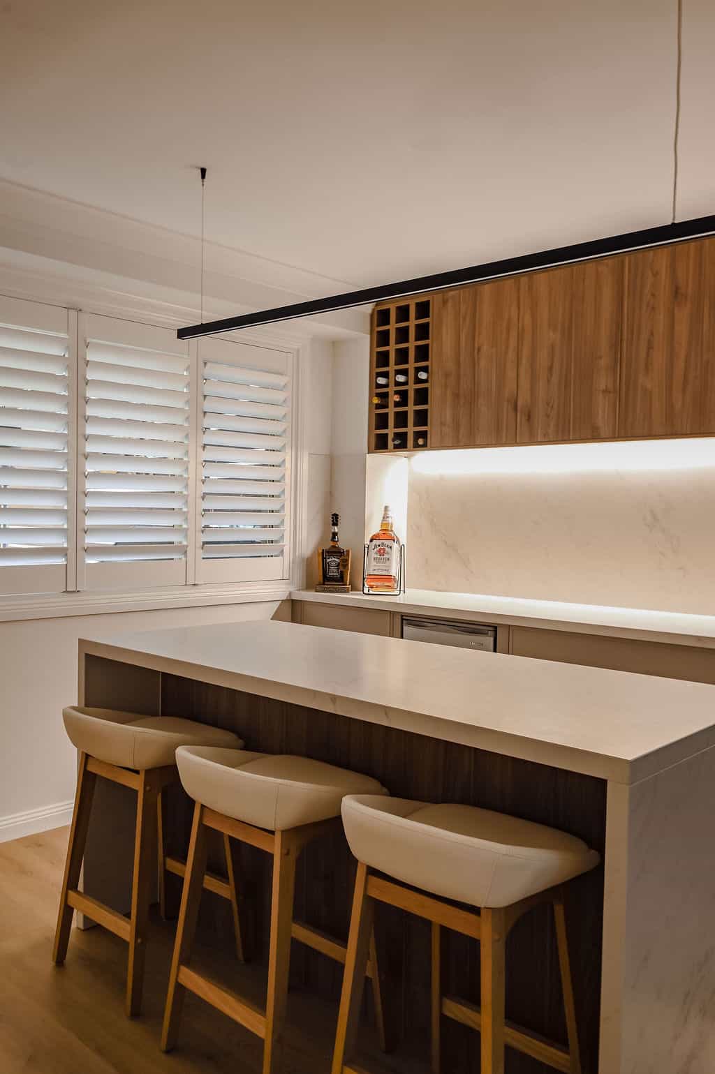 Showing white plantation shutters beside a modern kitchen with a stone island, timber cabinetry and warm lighting for privacy