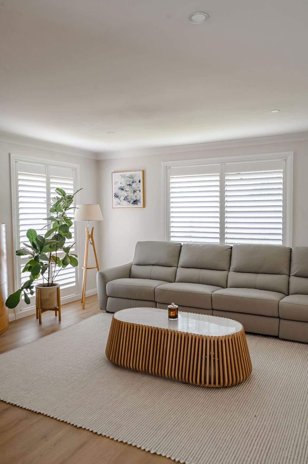 Showing white plantation shutters in a modern living room with a large sofa, timber coffee table and soft natural light.