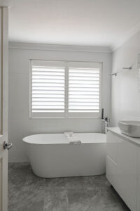 Showing white bathroom window shutters above a freestanding bath, providing privacy, natural light and a clean modern finish.
