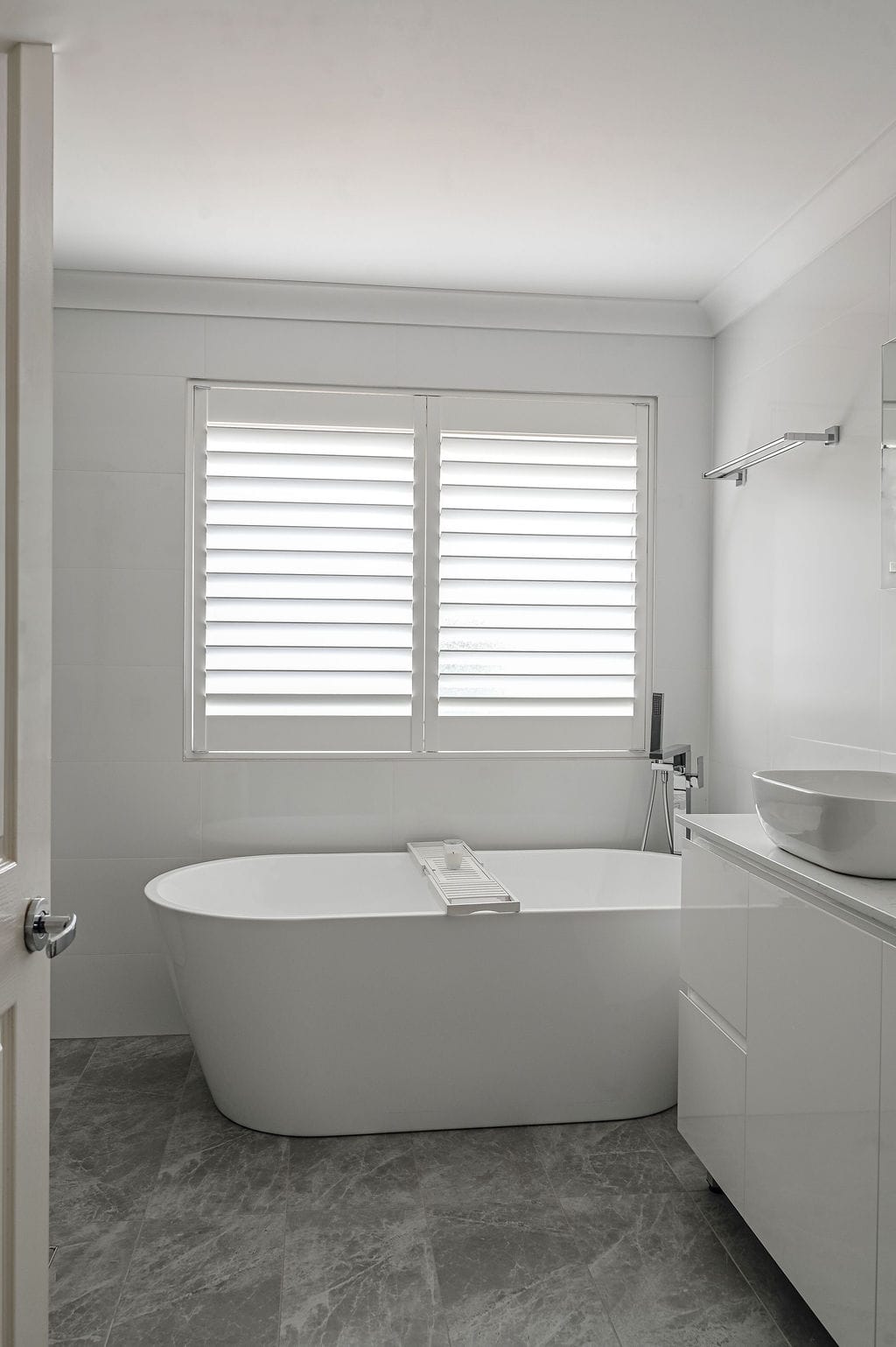 Showing white bathroom window shutters above a freestanding bath, providing privacy, natural light and a clean modern finish.